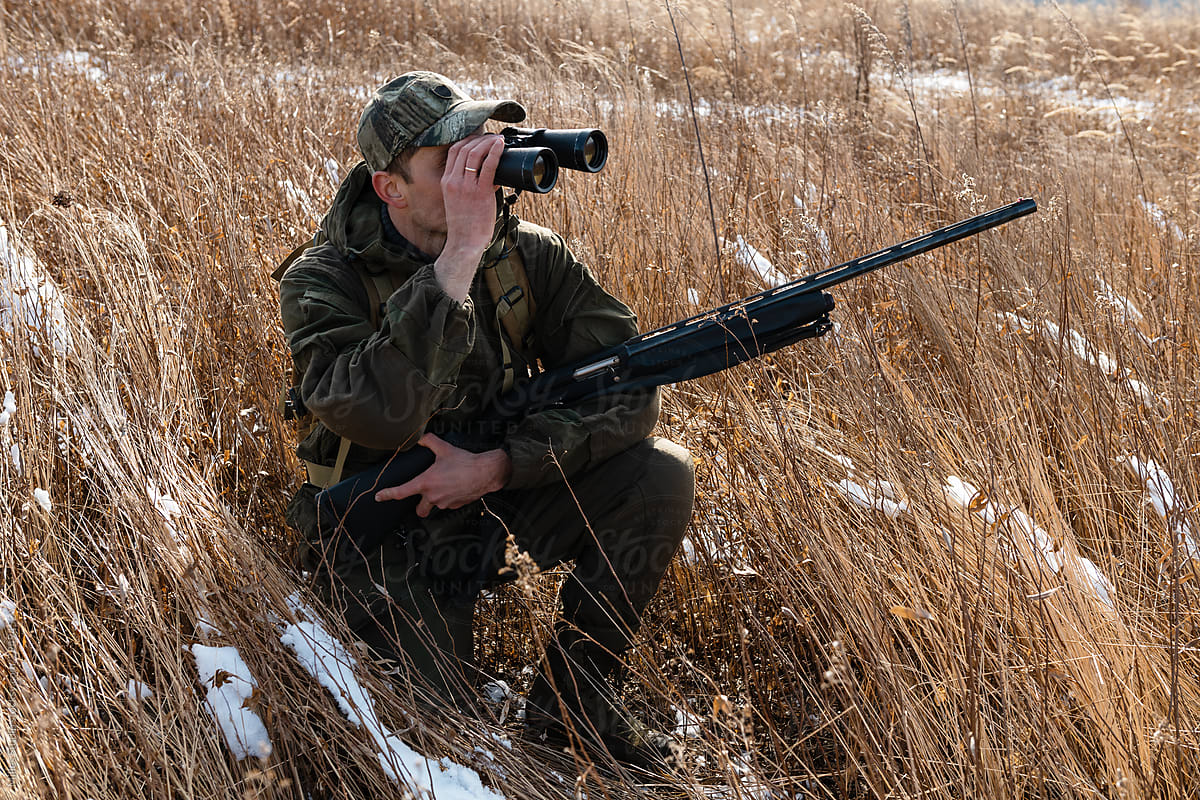 Hunter kneeling in field and using binoculars