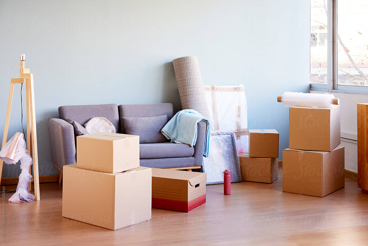 Stack of cardboard boxes with belongings on wooden floor near sofa