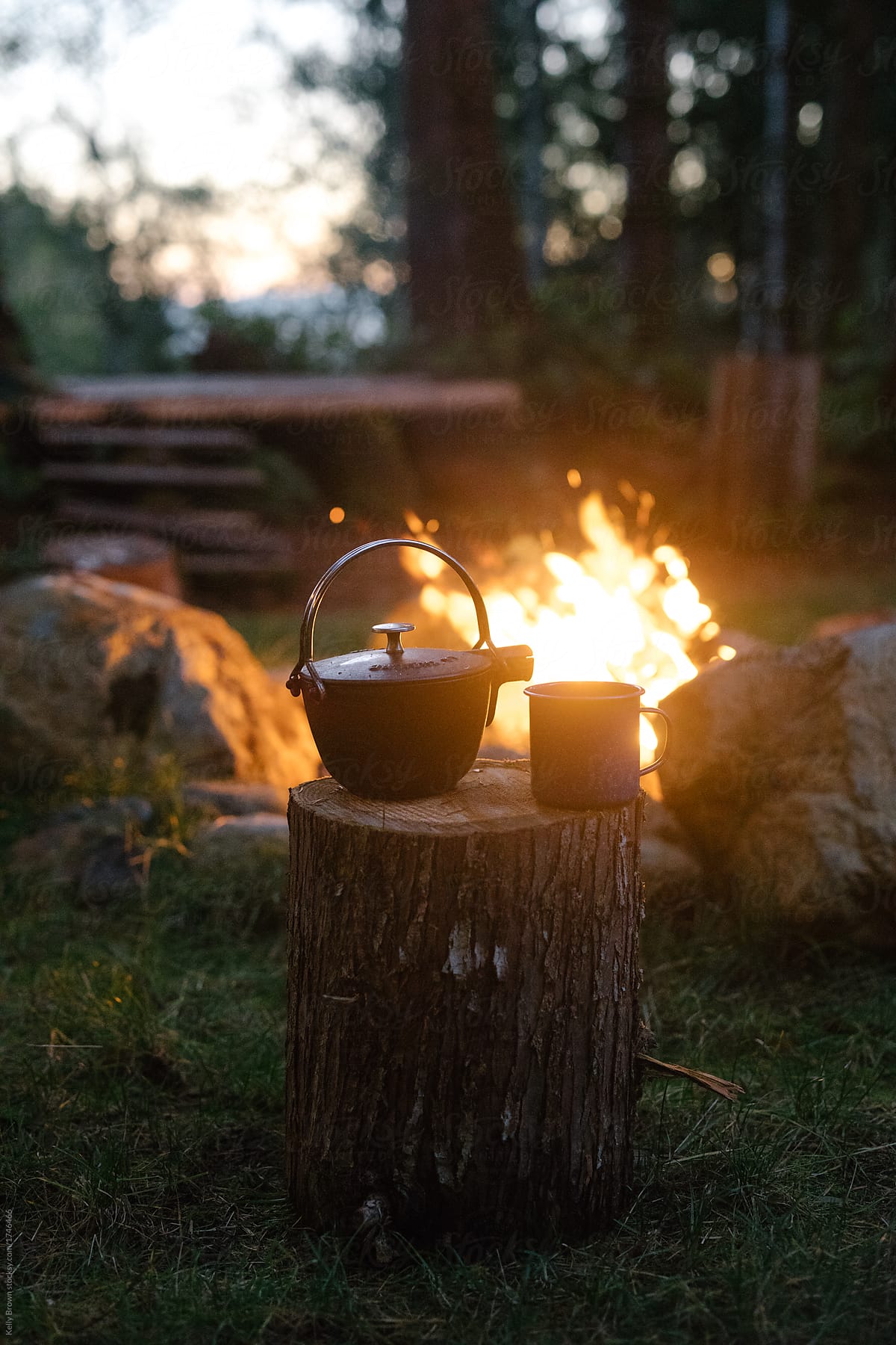 a campfire with a cast iron kettle and enamel cup