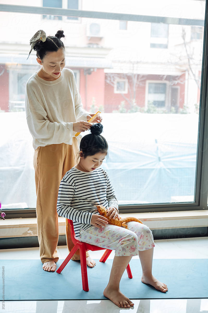 Mother styling hair of daughter at home with pets