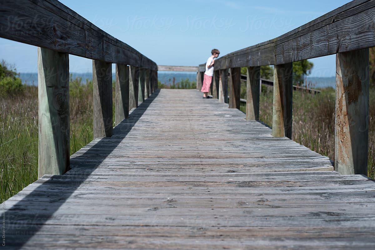 Boy looks over railing of a wooden walkway to the beach