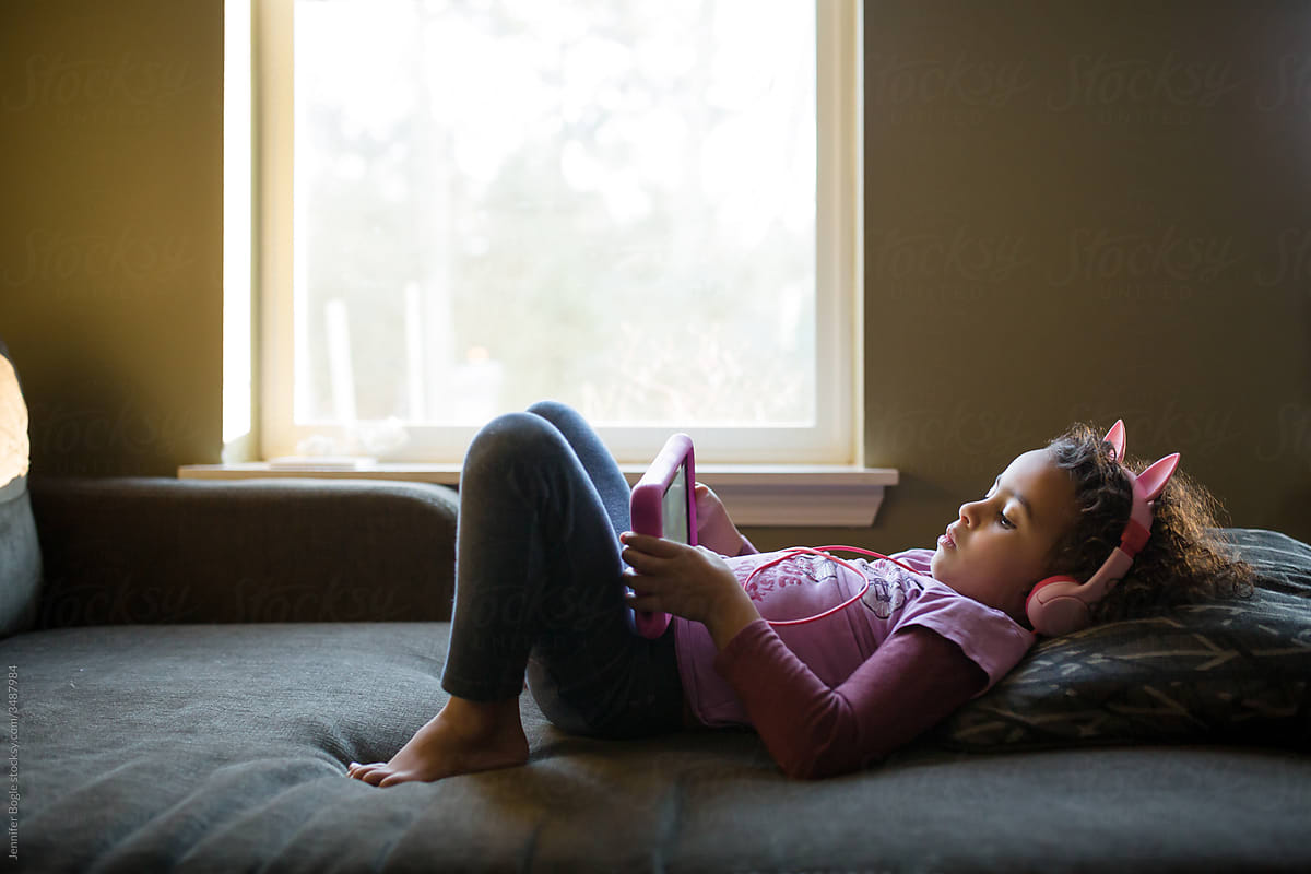 Girl with animal headphones lays on couch looking at tablet