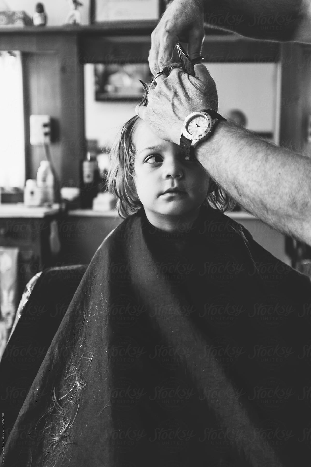A young boy looking up suspiciously at barber during haircut