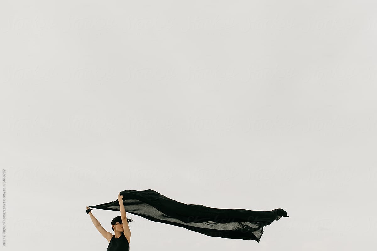 Woman holding black fabric as it blows through the wind