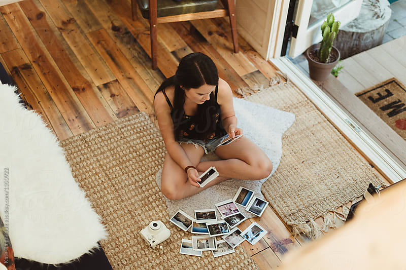 Young woman sits on floor of tiny home looking at polaroids