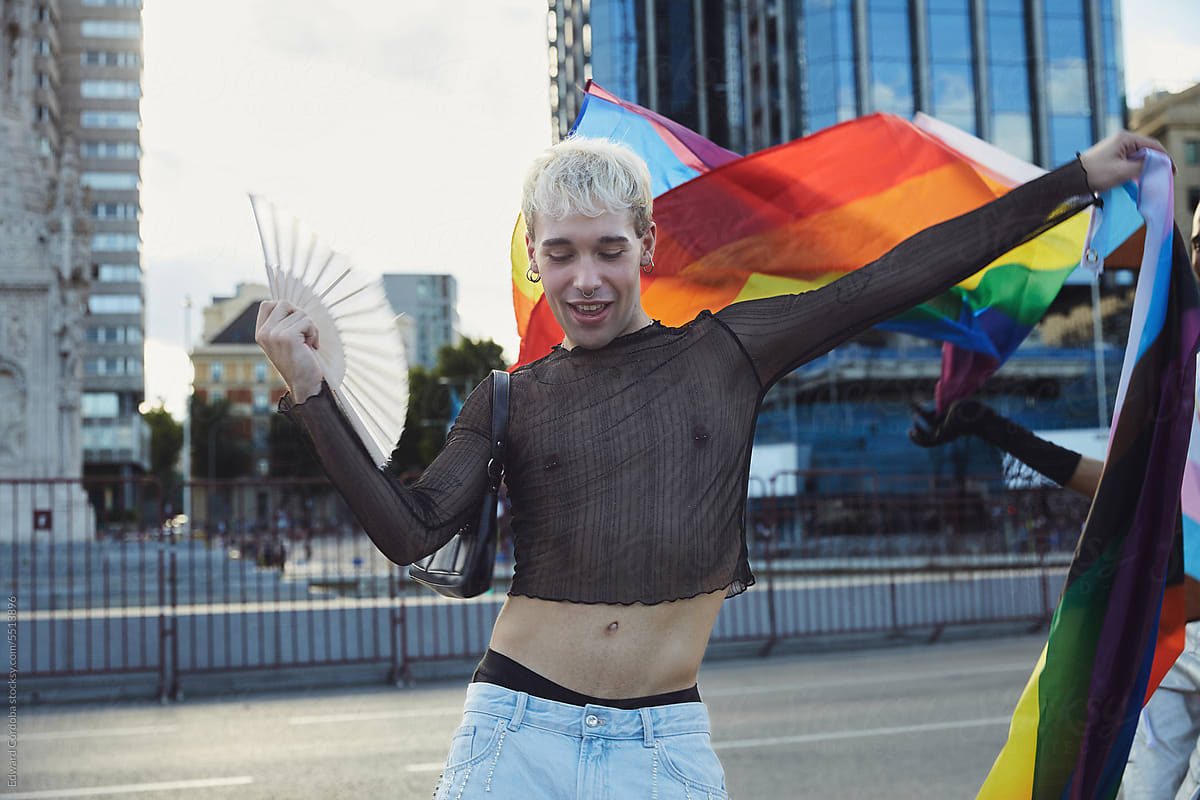 A young blonde guy proudly holding up an LGBTIQ+ flag.