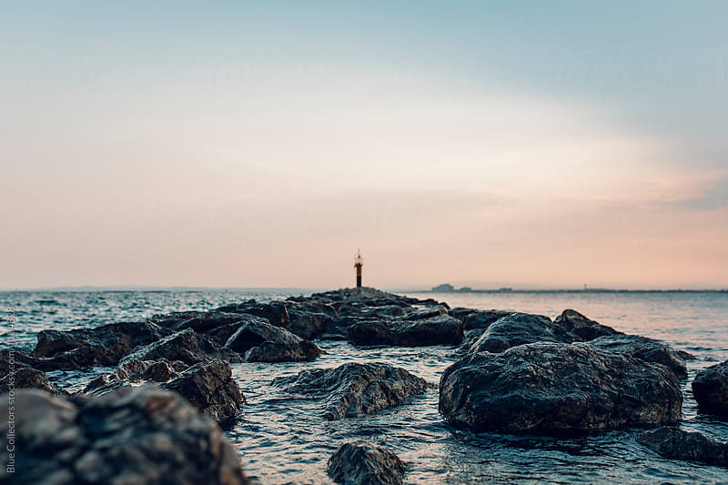 A lighthouse at sunset surrounded by water and rocky path, out of focus