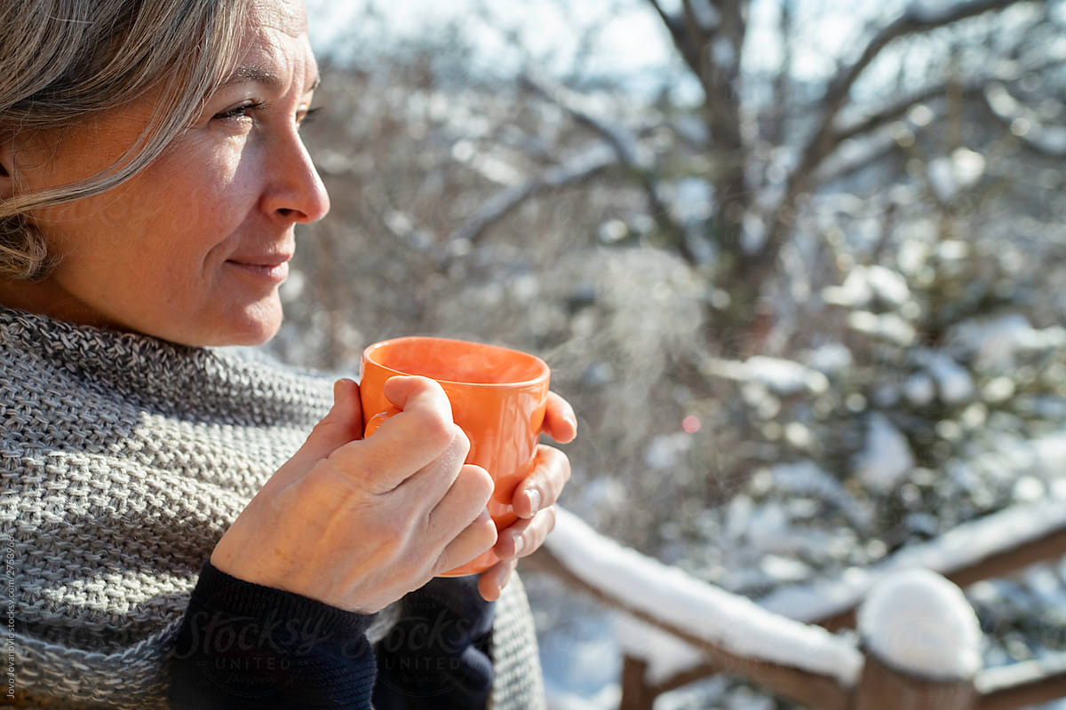 Older woman warming up with hot beverage outside in winter time