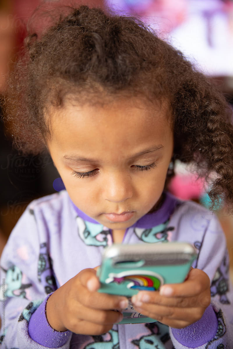 Preschool child with curly hair using an electronic phone
