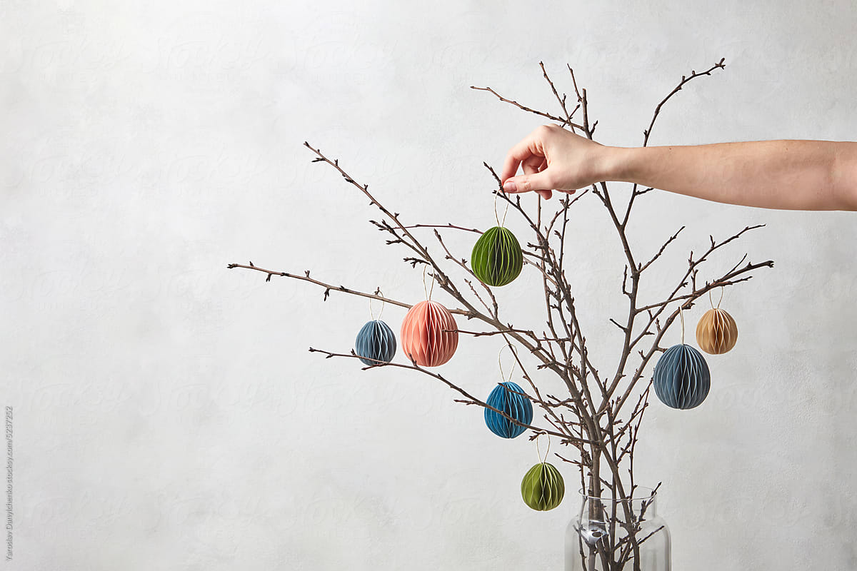 Paper Easter eggs hung by woman on tree twigs.