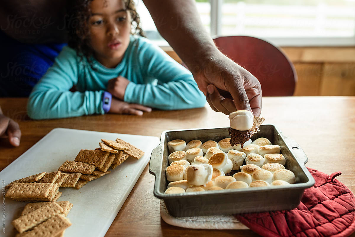 Daughter watches as dad scoops graham cracker into s\'mores dish