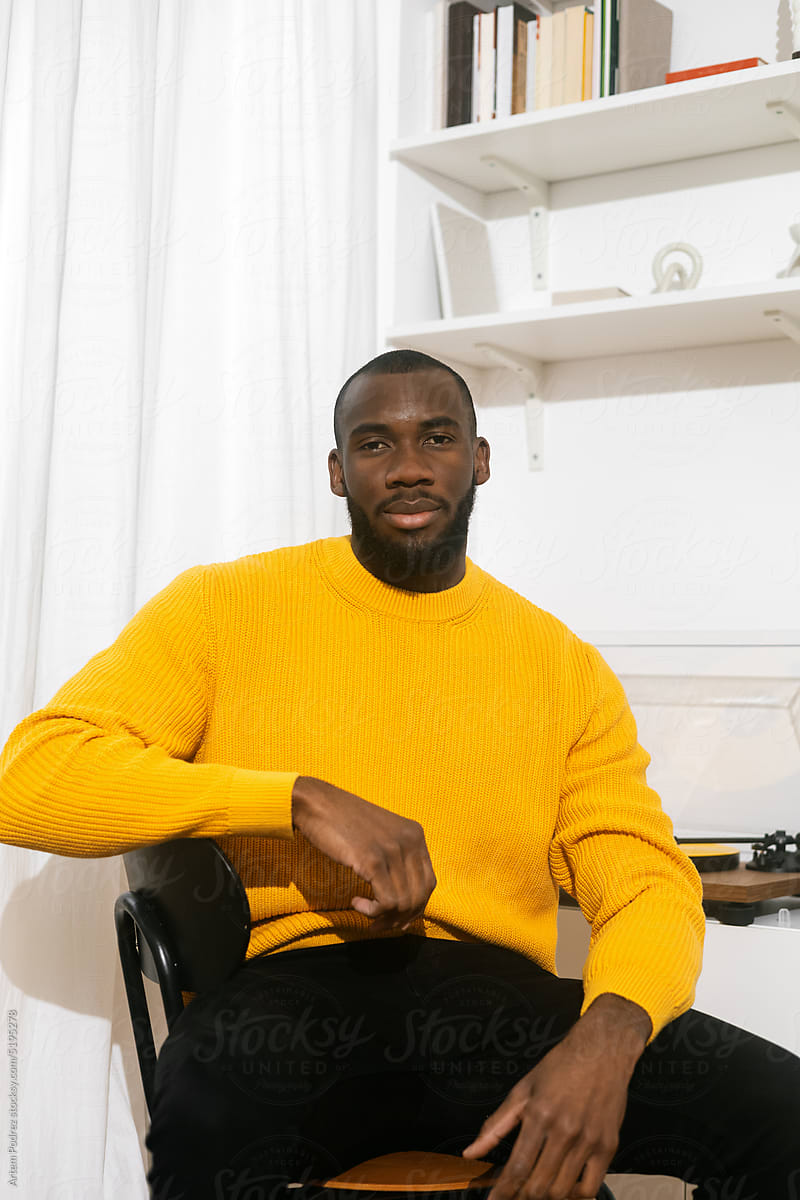 Portrait of a black man on a chair in a yellow sweater