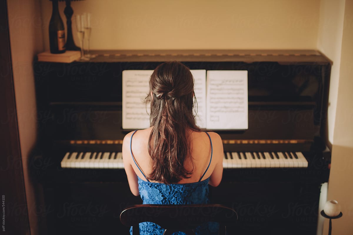 Young woman in blue dress playing the piano using a note sheet