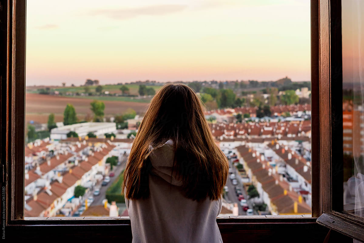 Teenager girl from back looking at city from the window