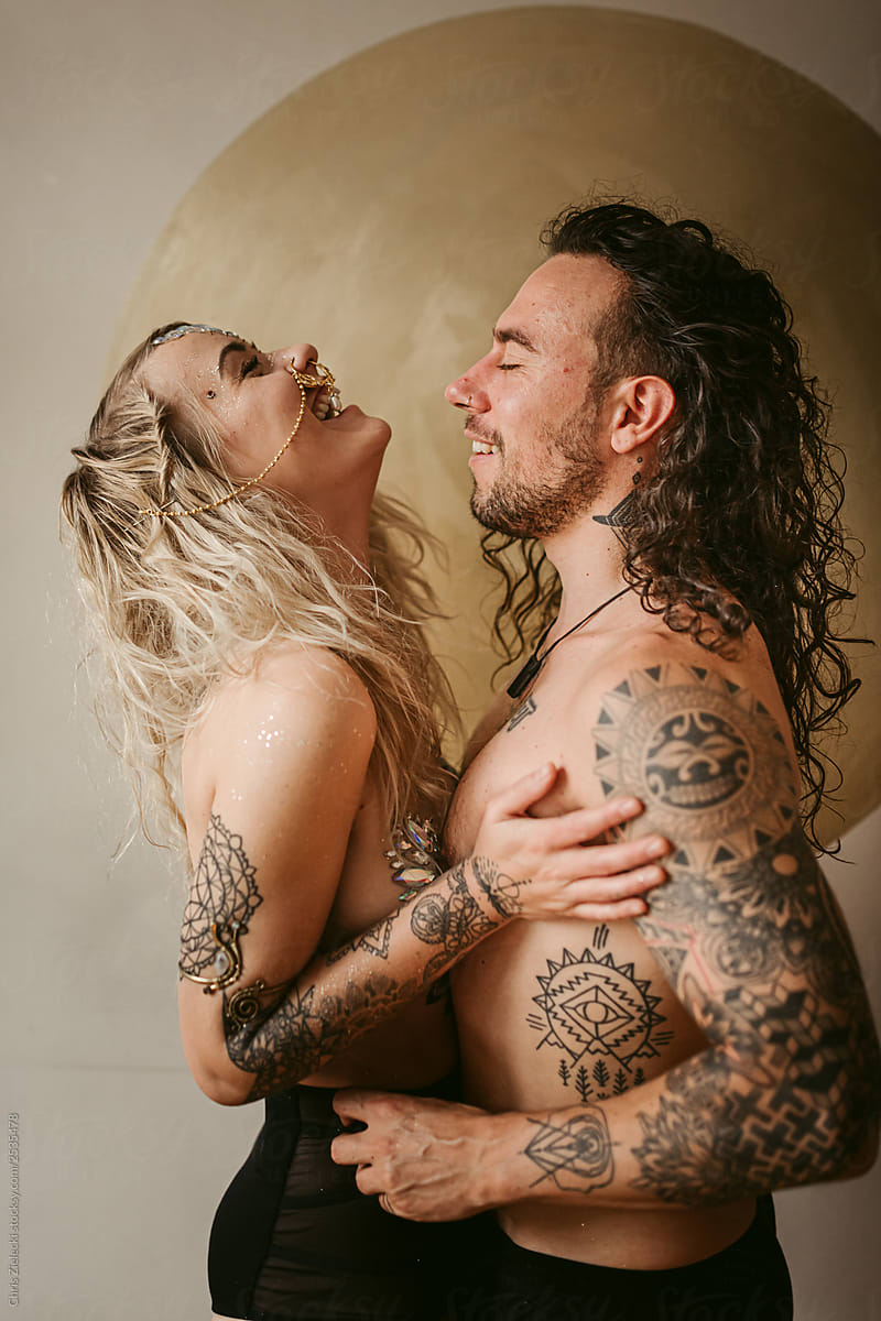 Happy couple with spiritual tattoos embracing near wall