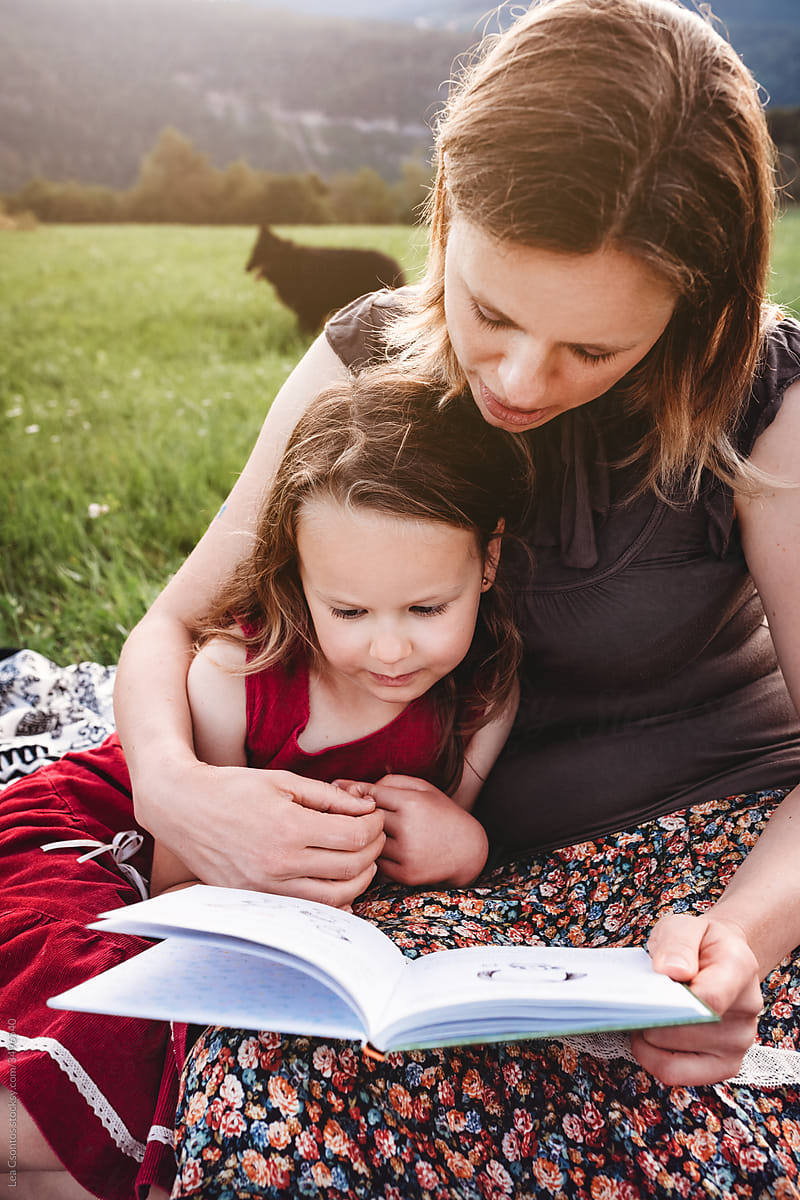 Mother and daughter reading a book outdoors