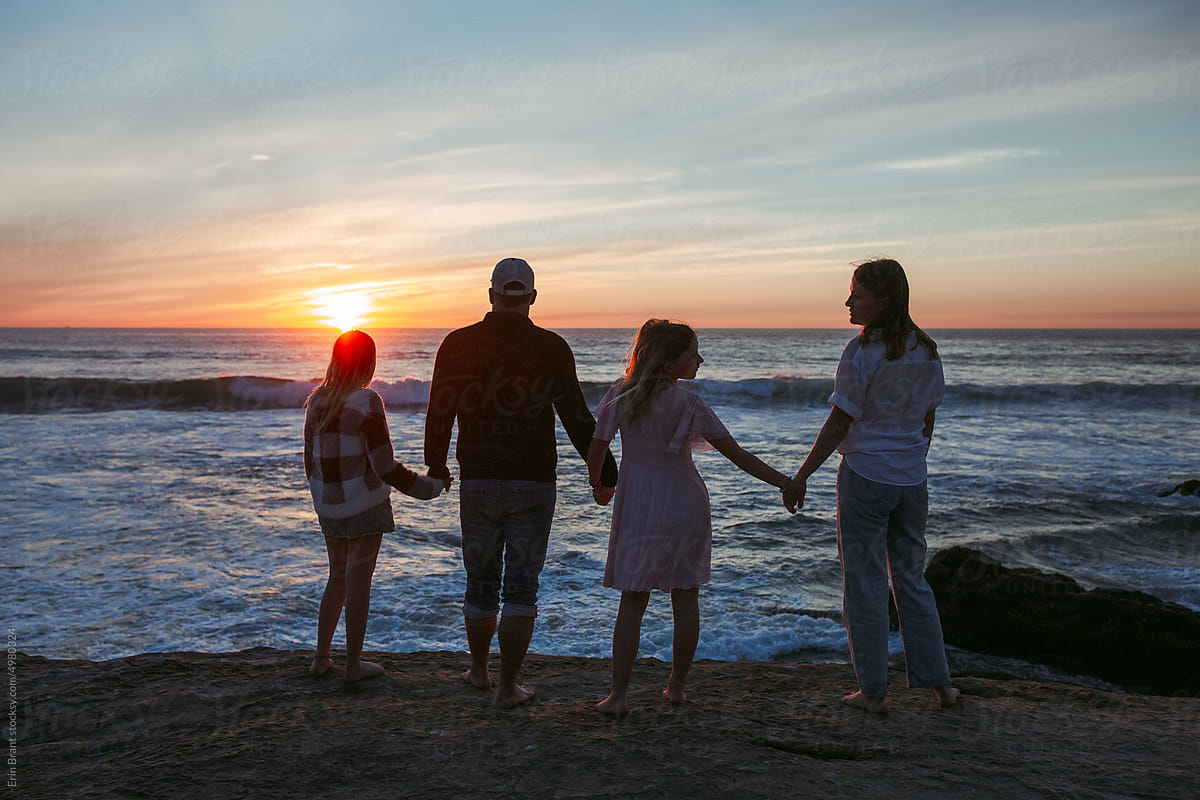 Family of with teenagers standing at the beach watching the sunset
