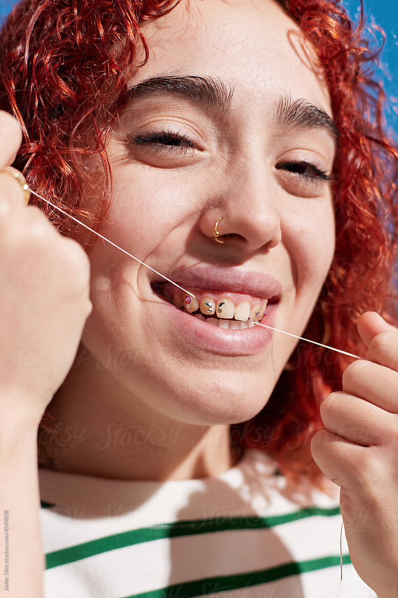Smiling redhead woman using dental floss