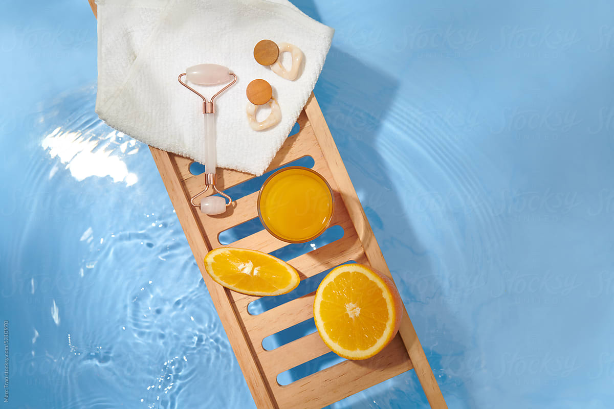 Roller face massager and fresh orange on wooden tray