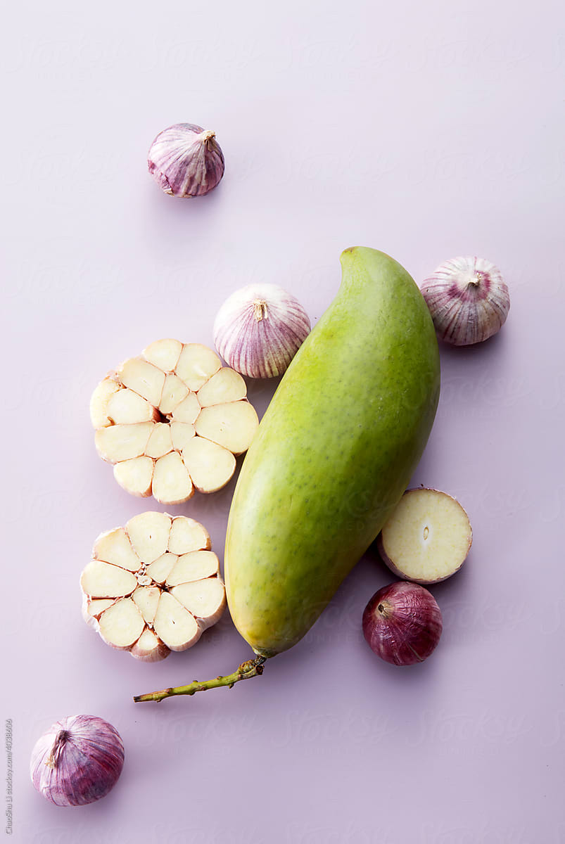 Closeup design arrangement of garlic and green mango, on lilac background