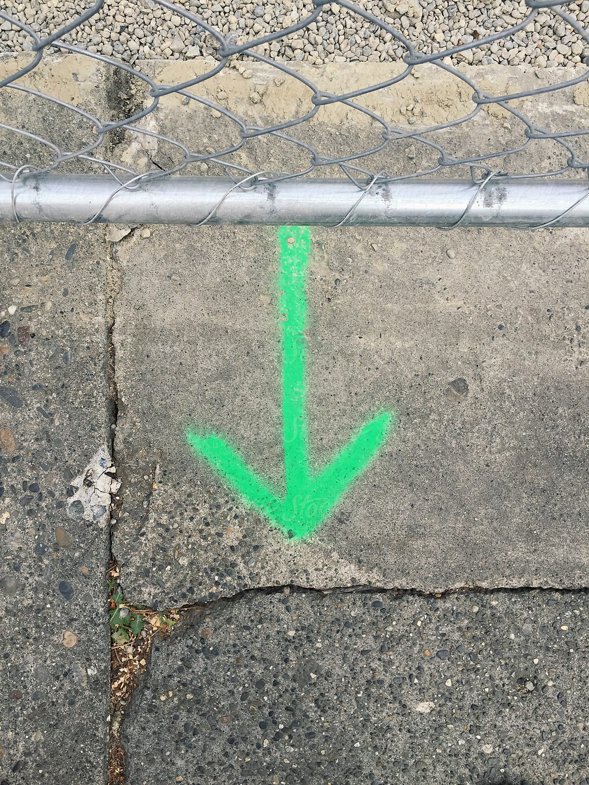 Green arrow painted on sidewalk, chain-link fence in foreground