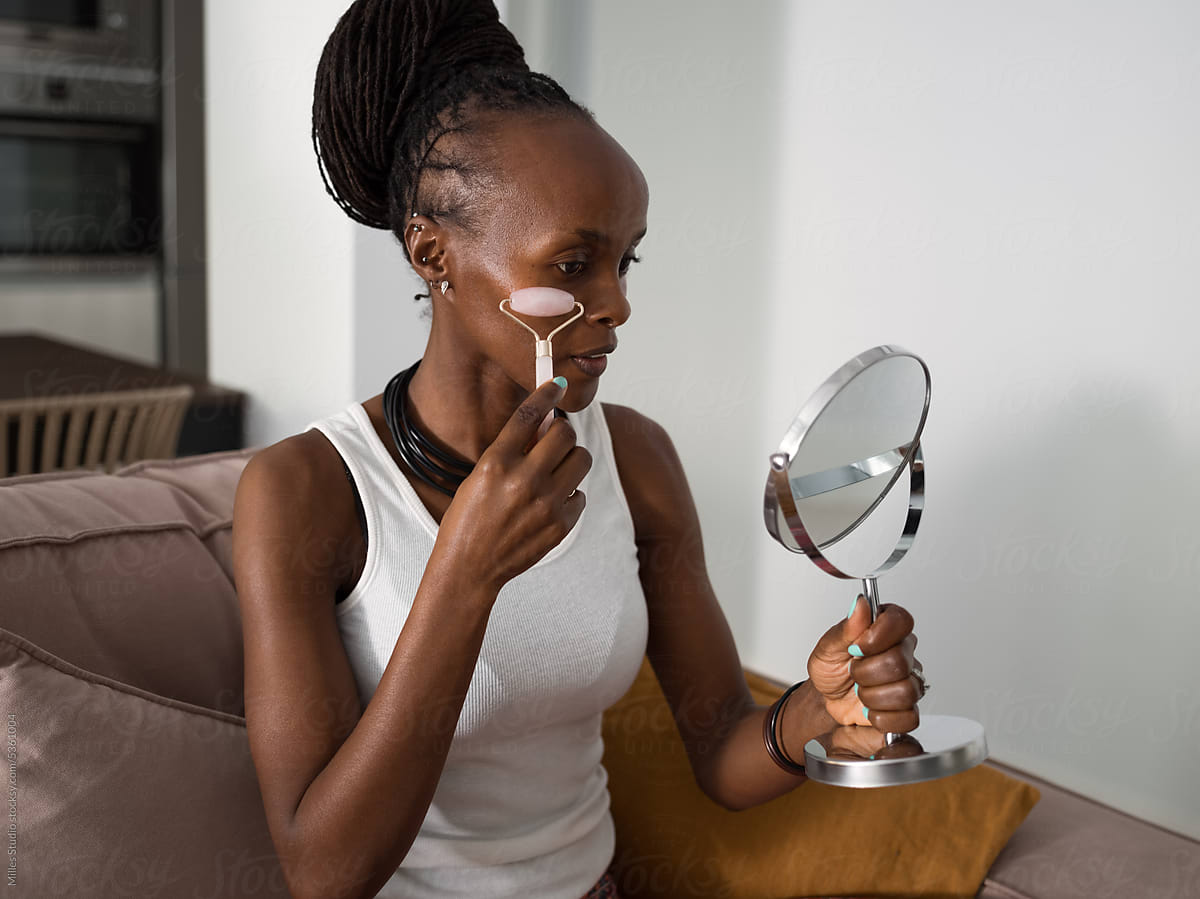 Black woman holding mirror while massaging face