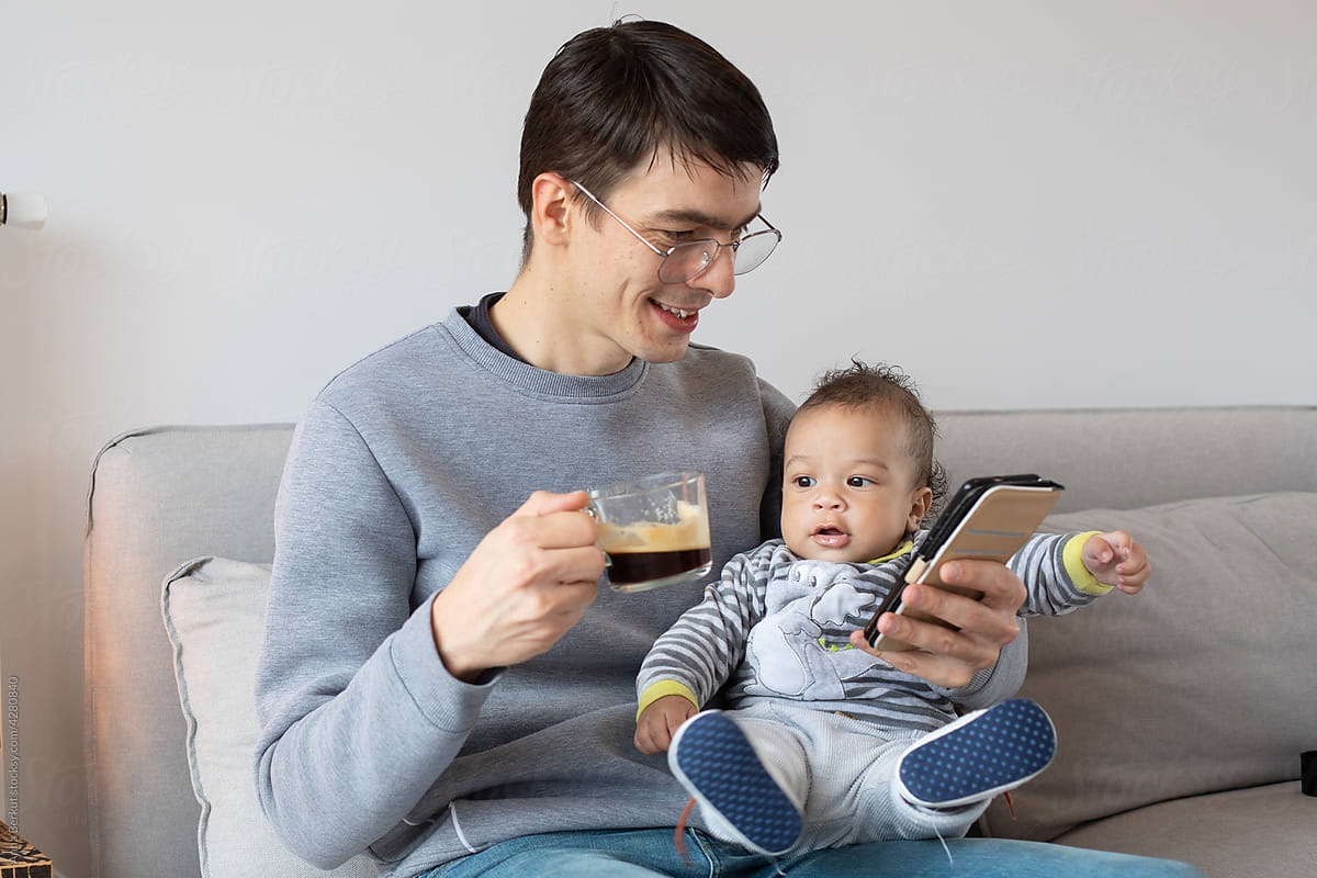 father reading emails on his phone while holding baby