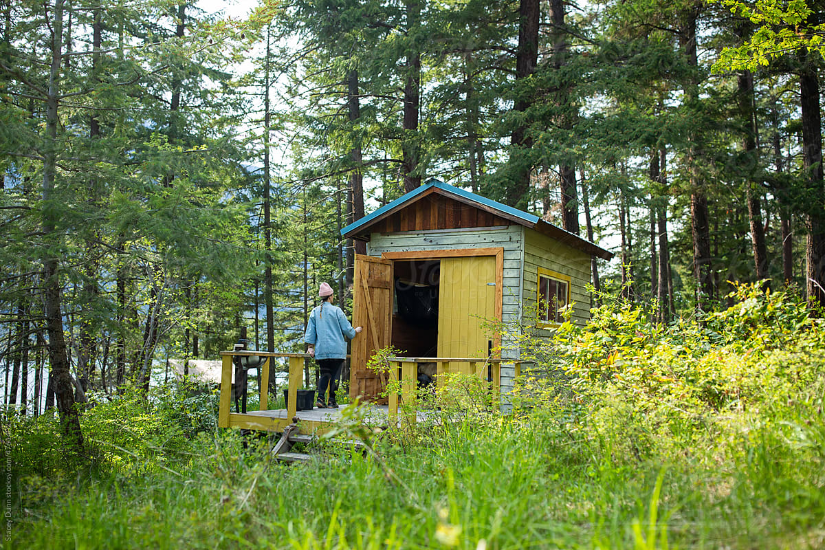 A woman standing on the landing of her tiny forest cabin.
