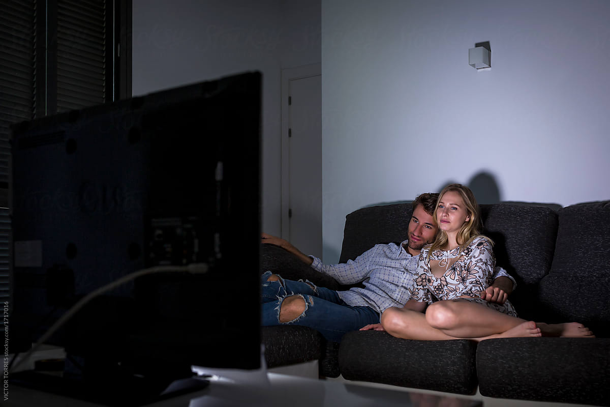 Happy adult couple watching TV at night lying on the couch