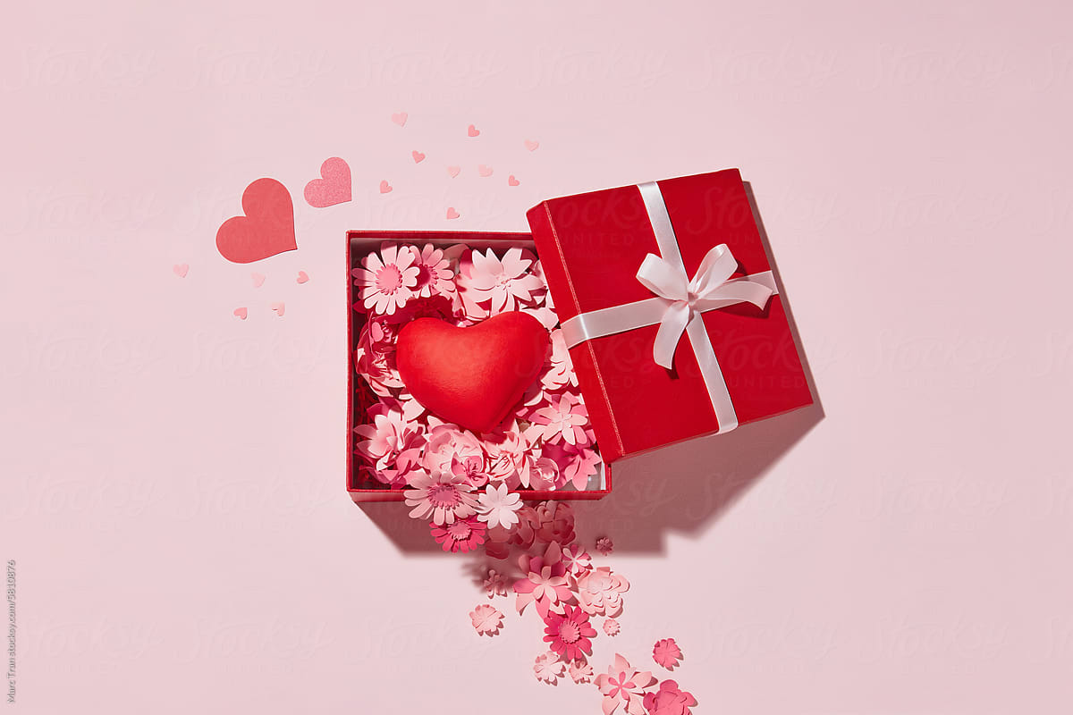 Paper art flowers in open gift box on pink background with red heart