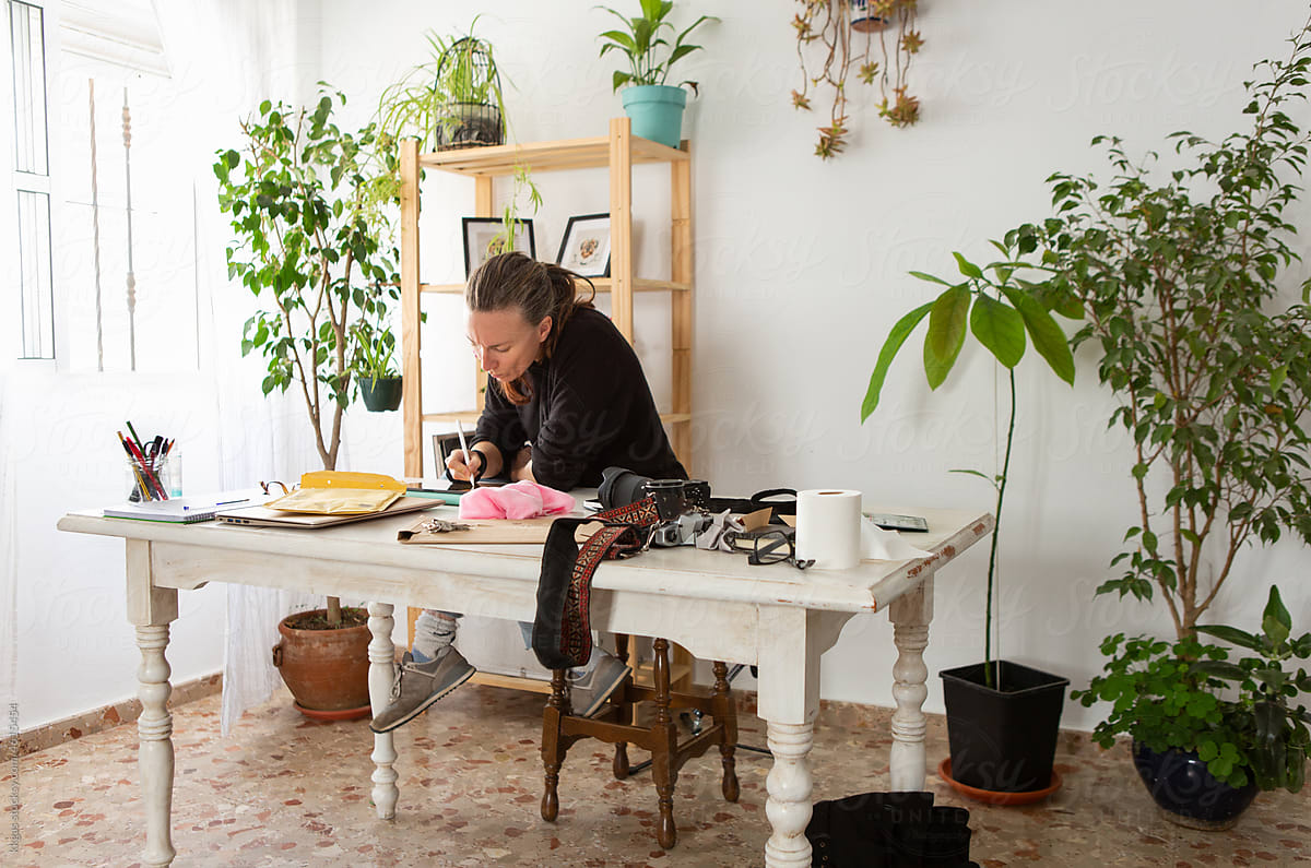 Woman works at a desk in a house plant filled home office