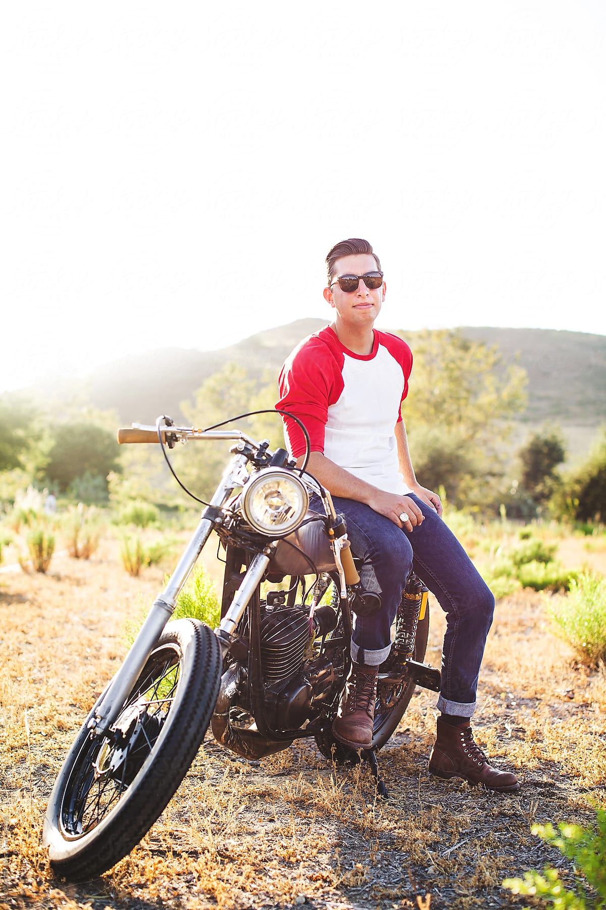 Young stylish man on a custom built motorcycle looking out on a meadow.