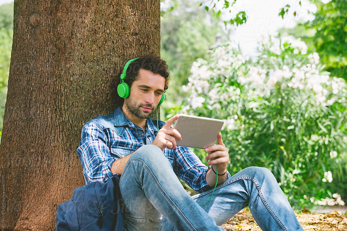 Young handsome man listenning music with digital tablet under a big tree.