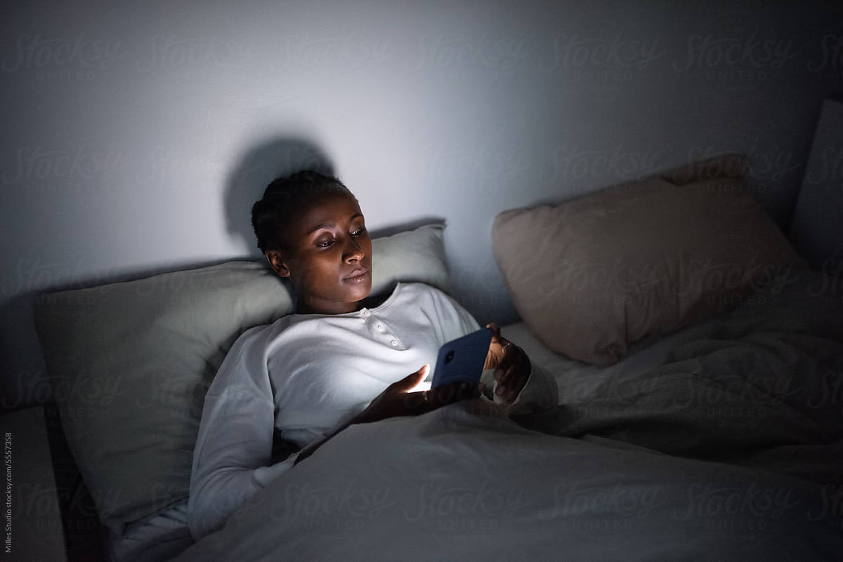 Black woman lying in bed using mobile phone