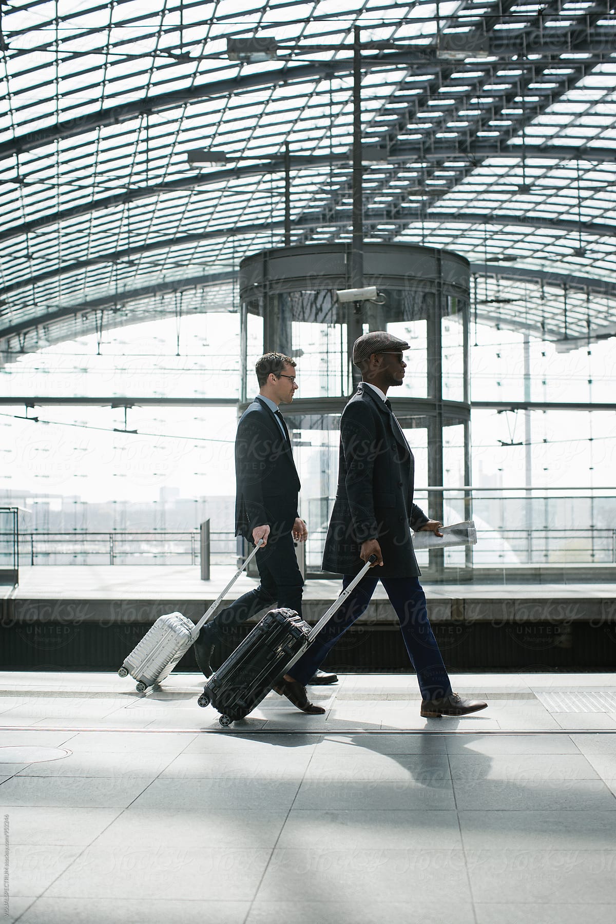 Two Young Business Travelers Walking With Carry On Suitcases in Modern Train Station