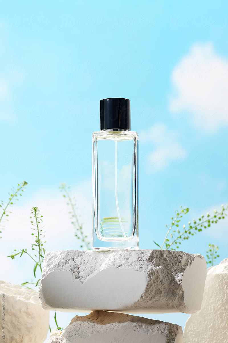 Glass perfume bottle on white podium over sky