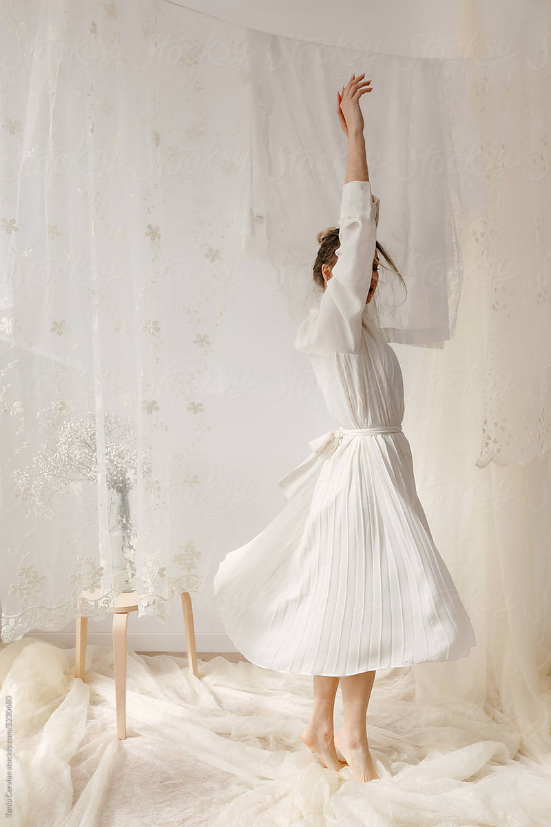 Graceful woman dancing on white light fabric in studio