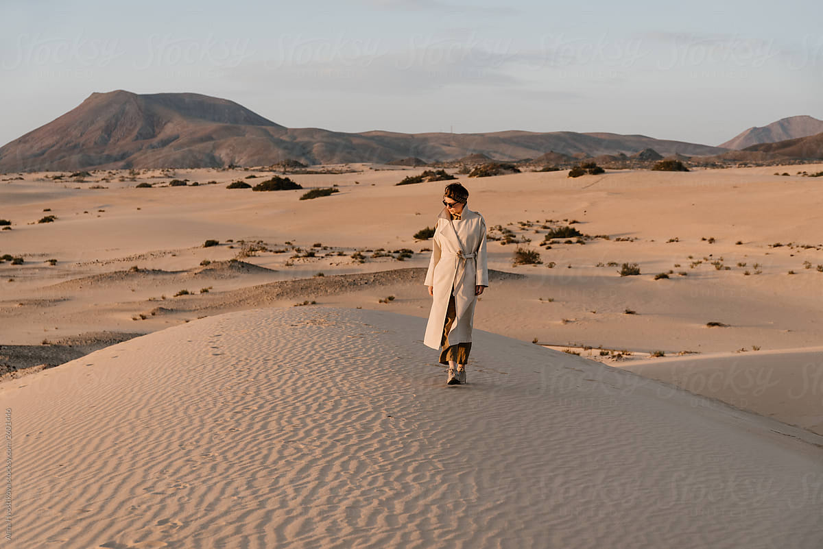 Woman in beige trench coat walking in desert.