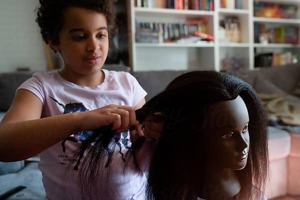 Girl Learns To Braid Hair On Black Mannequin Head by Stocksy