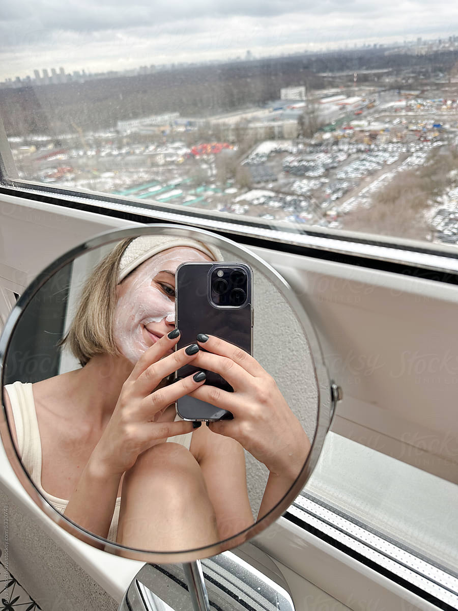 Young woman taking selfie in the mirror with beauty mask
