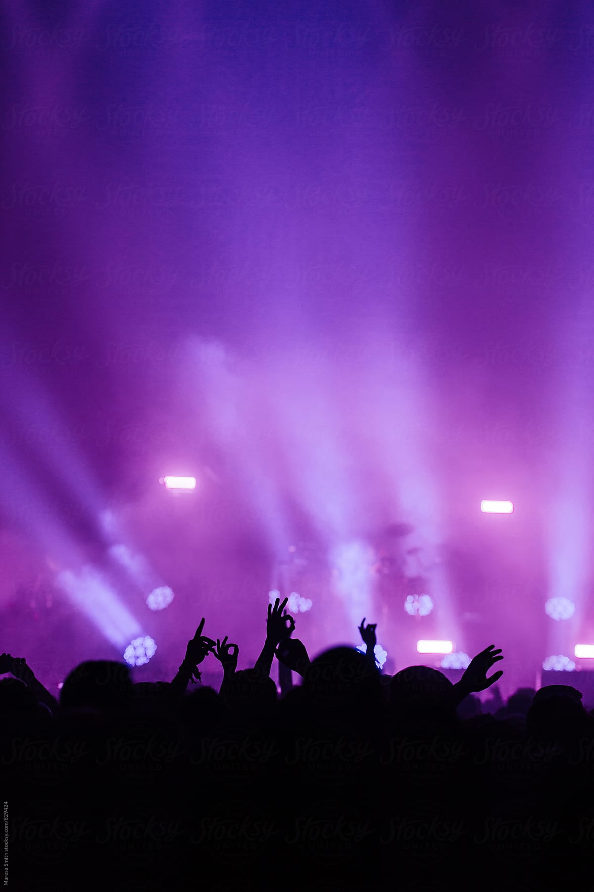 Purple and blue stage lights above a crowd of hands in the air gesturing \'ok\'