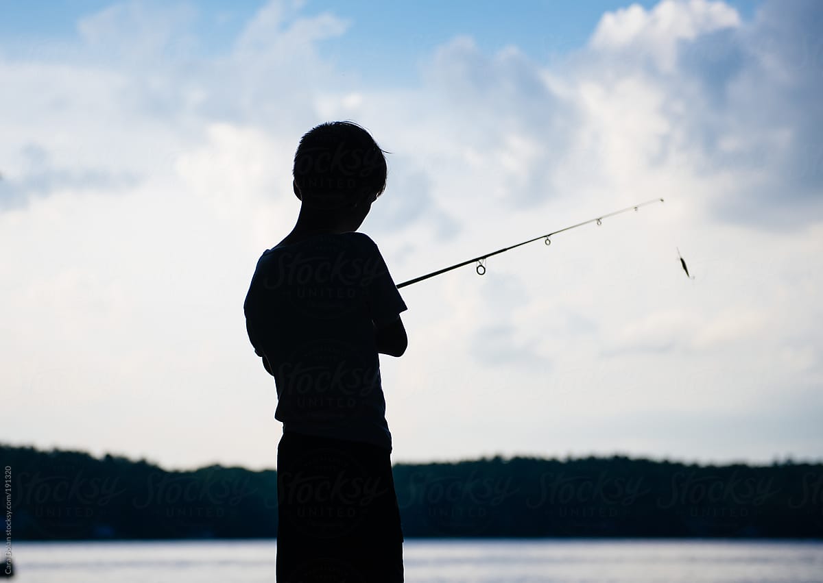 Silhouette Of A Boy Fishing On A Lake At Sunset by Stocksy