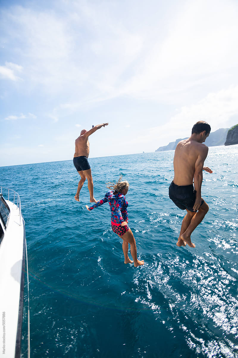 Happy people jumping off boat to ocean