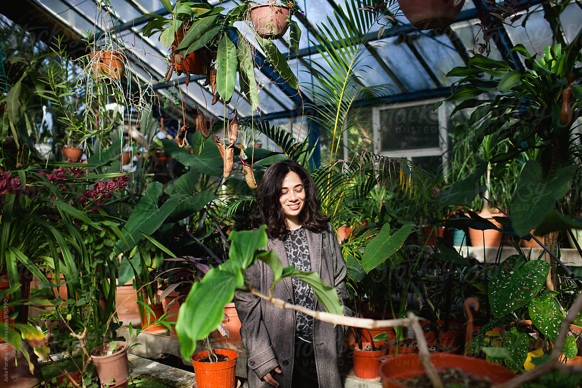 Woman looking down and smiling to herself as she walks through plants in a glasshouse.