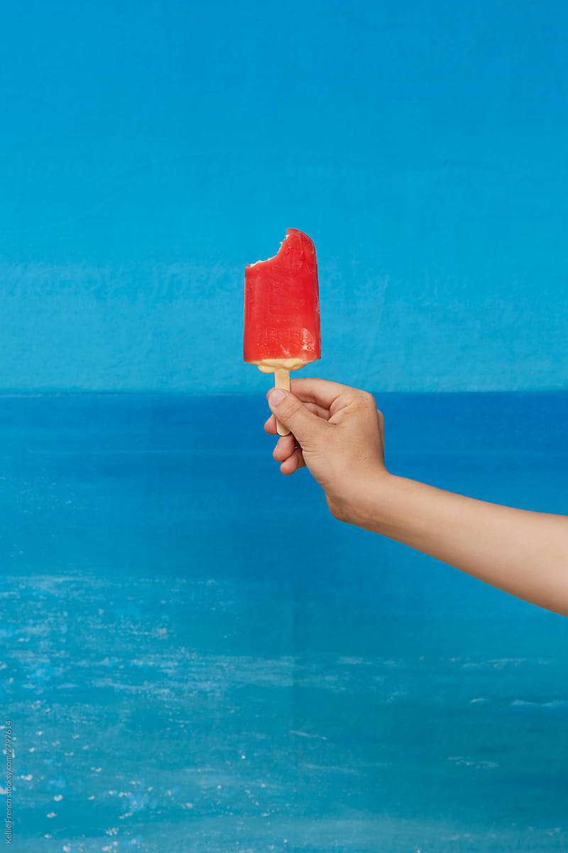 Child holds strawberry lollipop against a painted background of sea on a beach