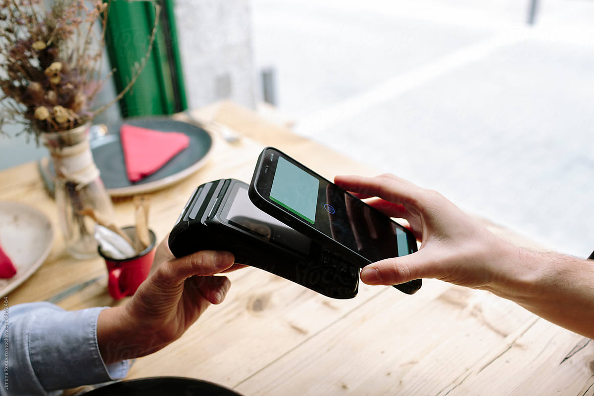 Detail shot of hand holding a smart phone doing a wireless payment at a restaurant