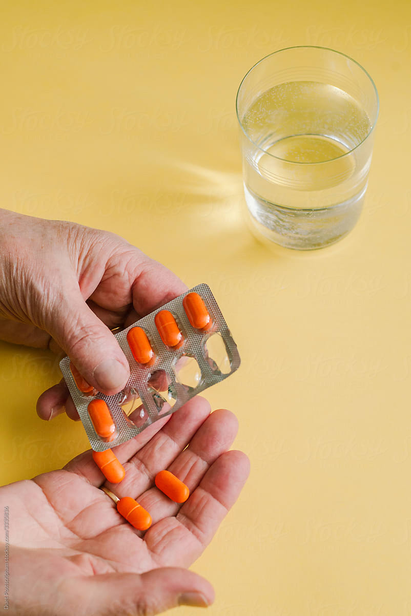 Hands of an elderly woman hold pills on a bright yellow background