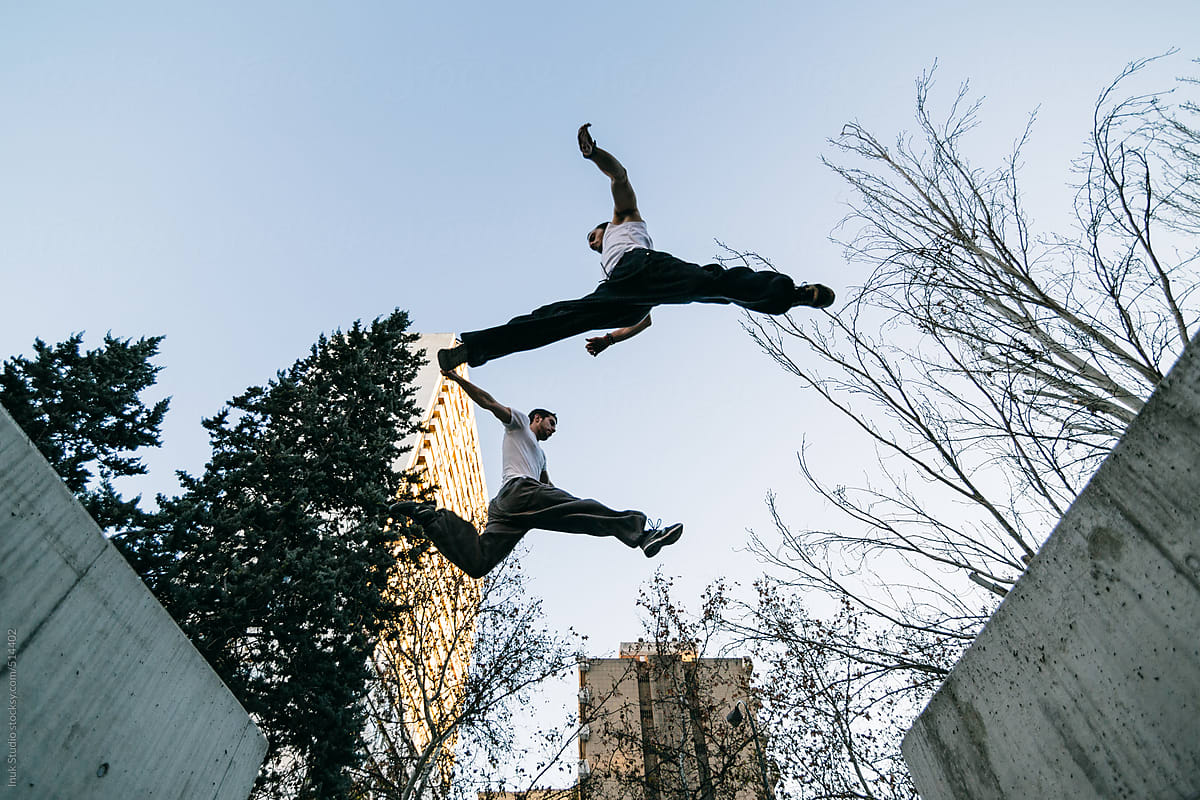 Two men jumping during a parkour training at sunset