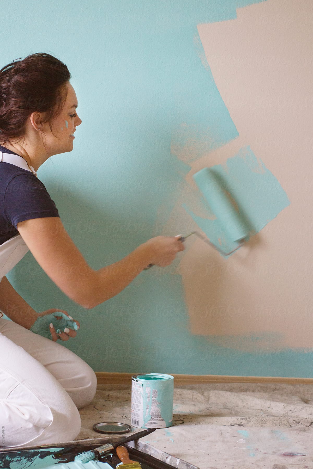 young woman rolls paint roller across wall