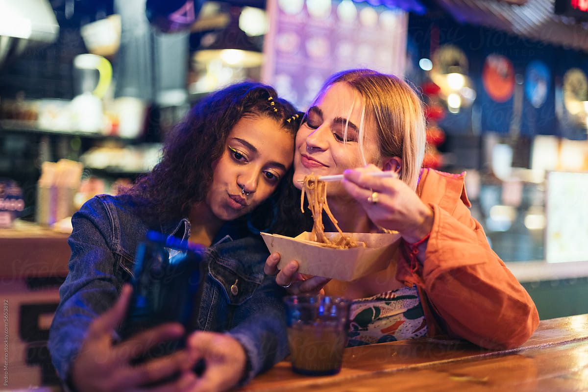 Young women in a date taking selfies while eating street food
